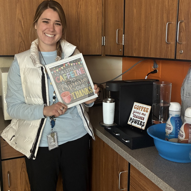 Mrs. Finnander holding a sign up by the coffee machine 