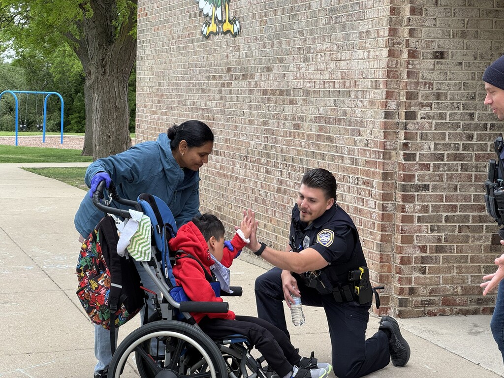 Police officer giving a high-five to a student outside of school.
