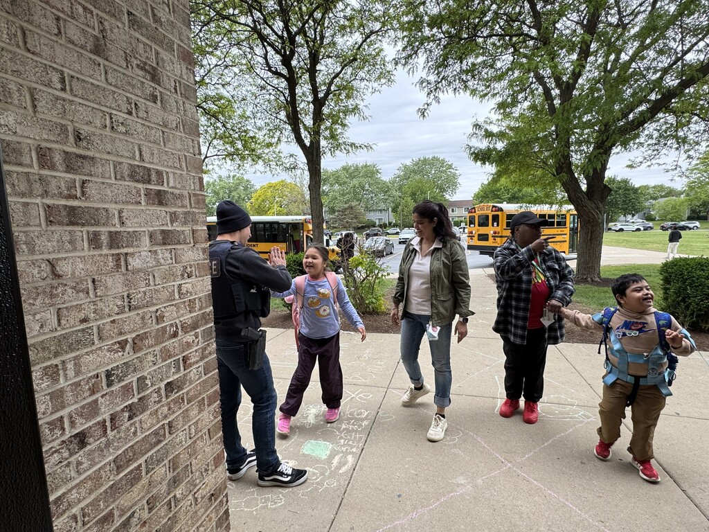 Police officer giving a high-five to  students outside of school.
