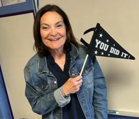 Mrs. Bouchard against a whiteboard holding a black "you did it" pennant sign
