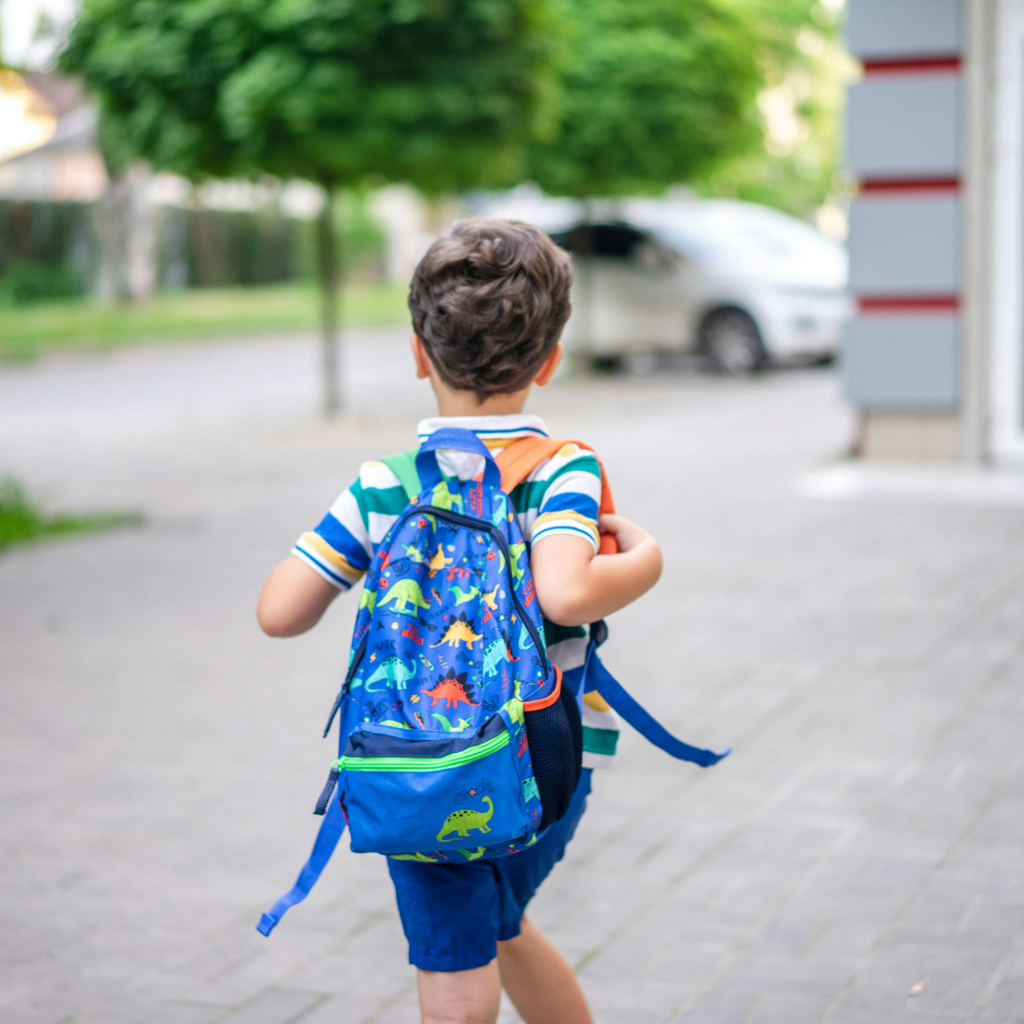 Student running towards school wearing blue dinosaur backpack