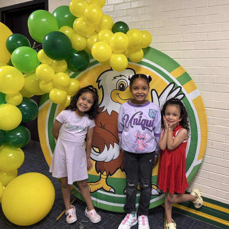 3 students smiling in front of a balloon arch and sign.