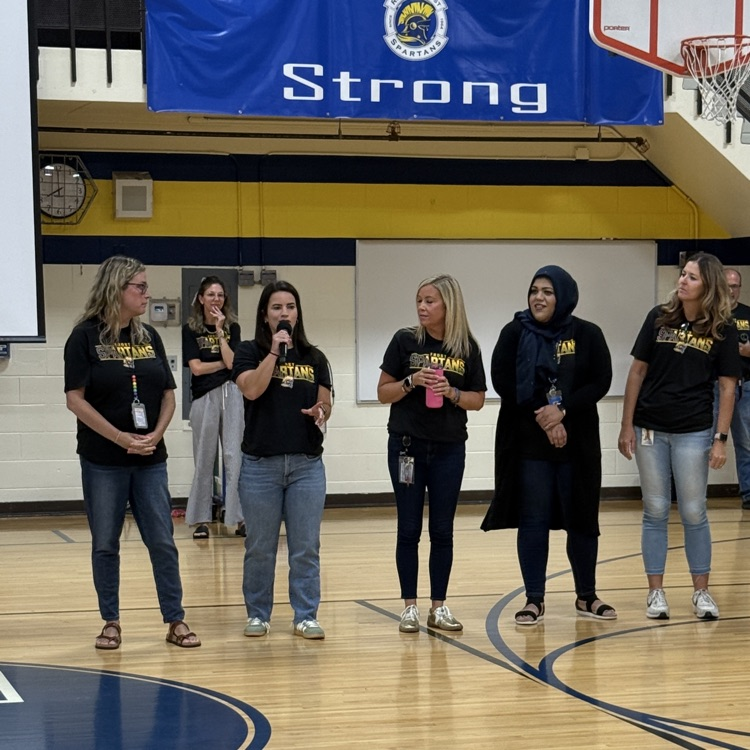 five women in gymnasium with microphone