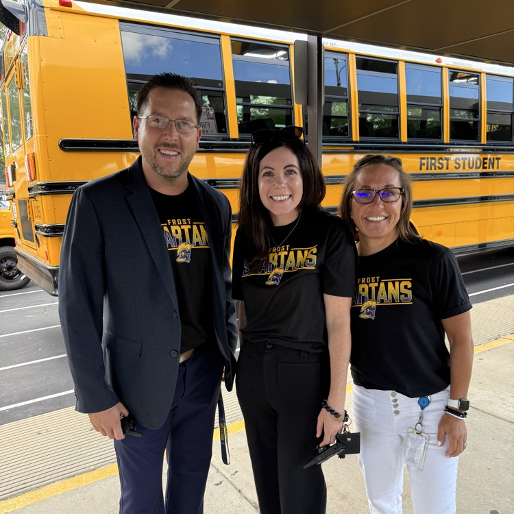 three adults standing in front of a school bus