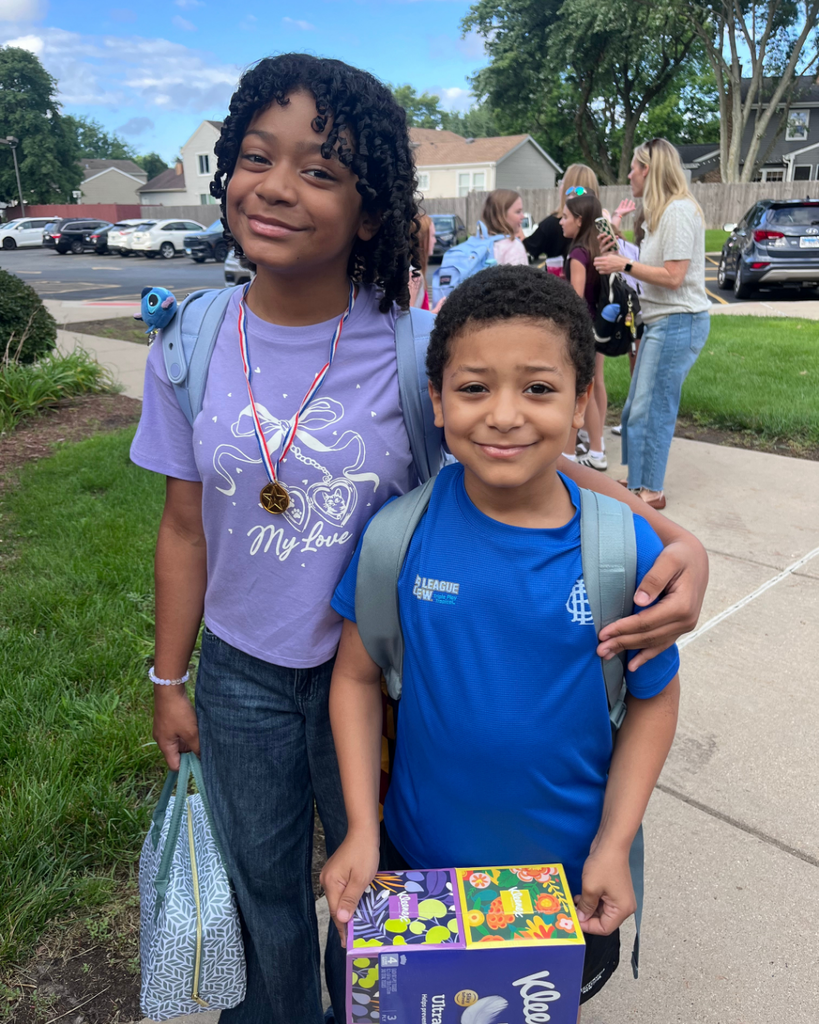 Siblings smiling together outside with backpacks on before their first day