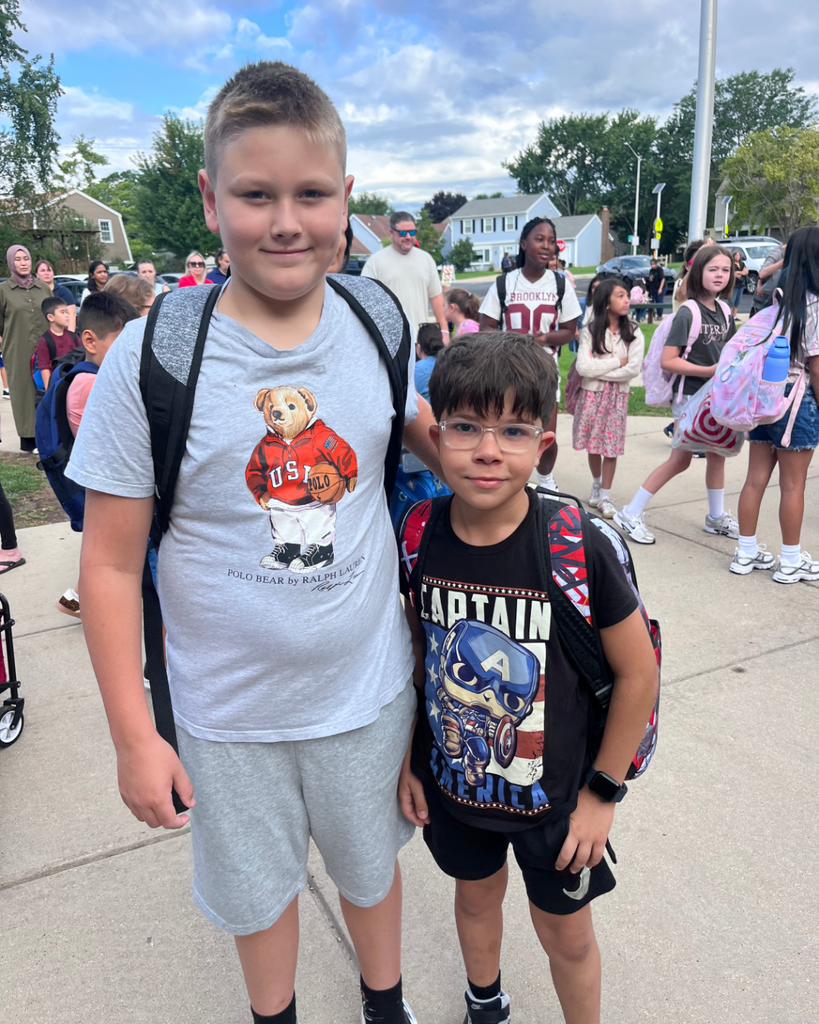2 student boys smiling together outside with backpacks on before their first day
