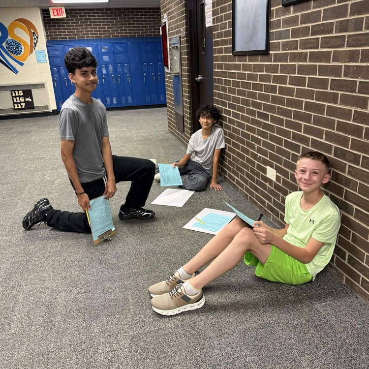 three teenage boys sitting in hallway with clipboards