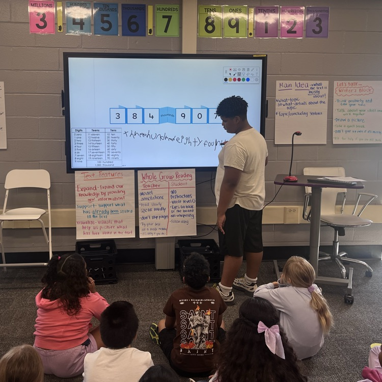 student modeling writing a number in word form for the class