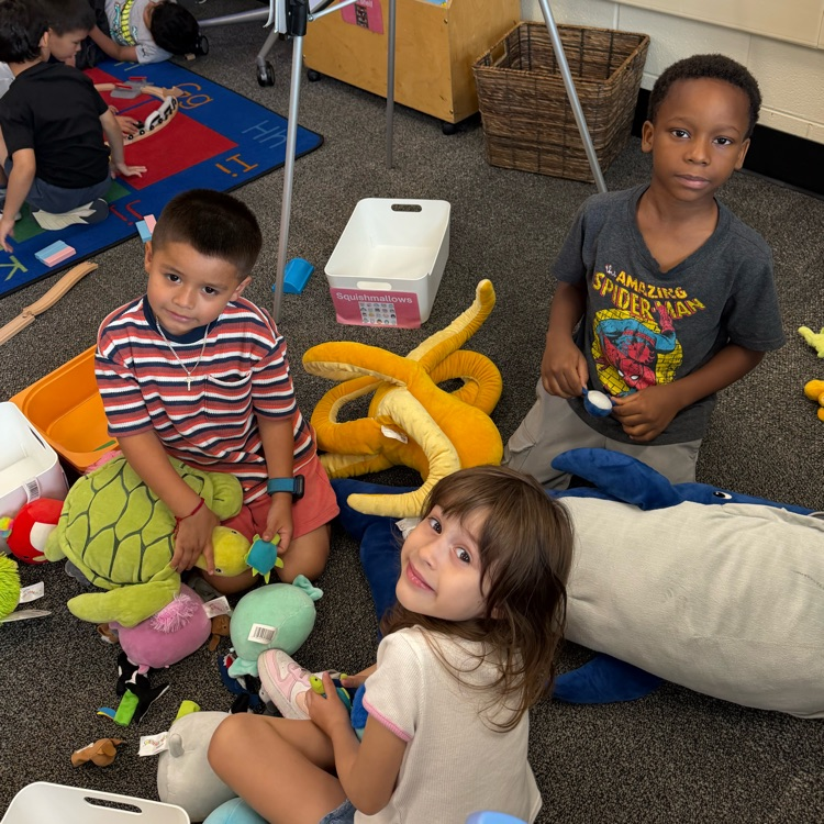 three students sitting on the carpet with stuff animals