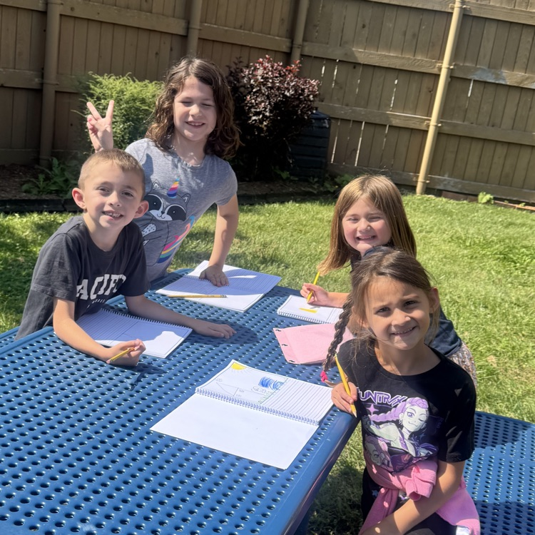 four students smiling for the camera as they write