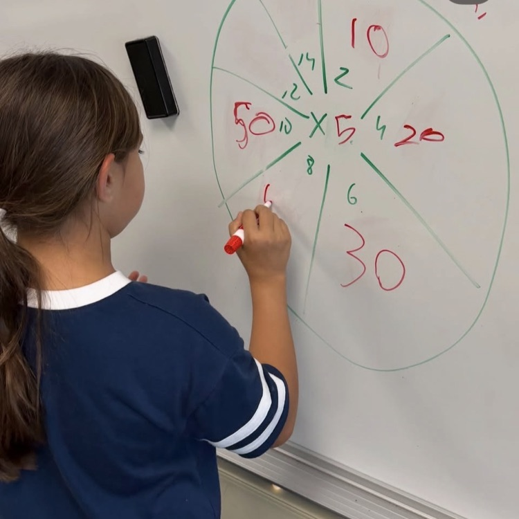 a girl solving a multiplication problem on the whiteboard 