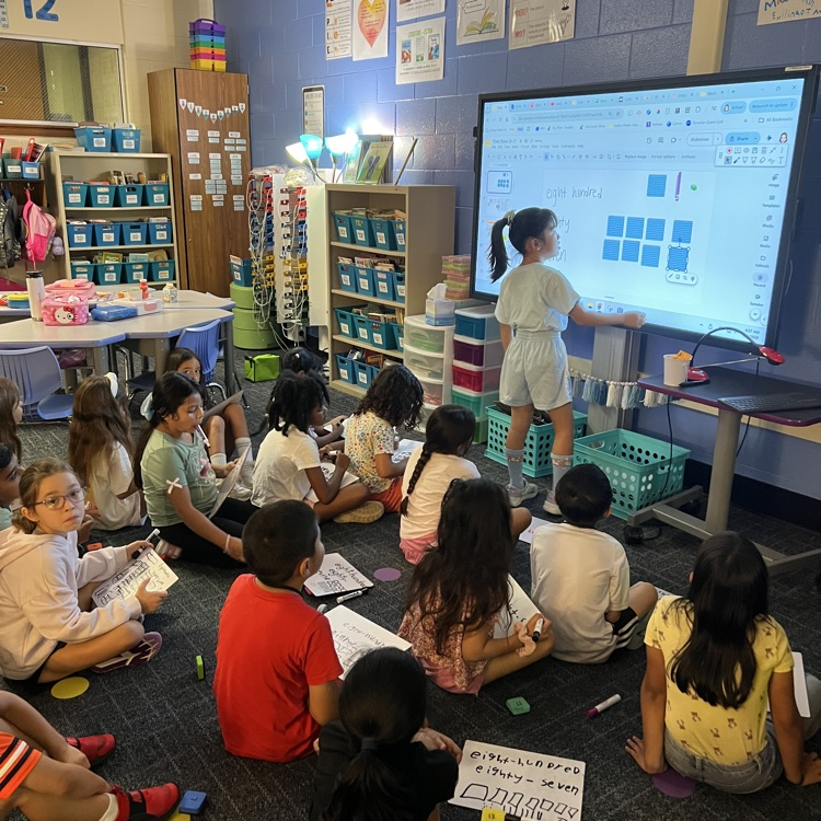 2nd graders completing math on dry erase boards with student showing her work on the monitor.
