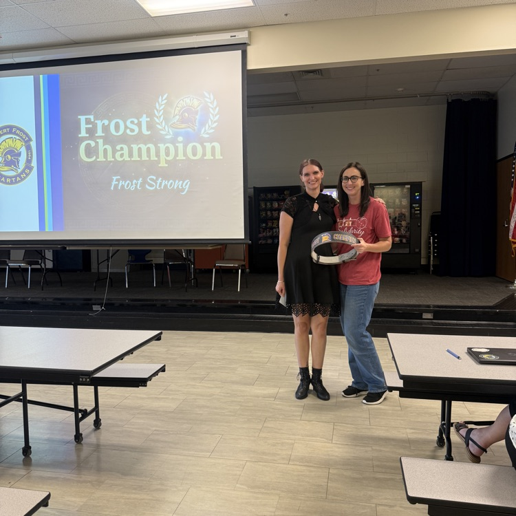 two women standing in a cafeteria holding a wrestling belt