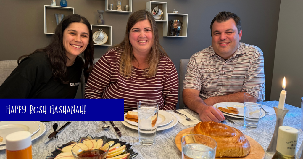 Happy Rosh Hashanah! Family sits at table together with apples and honey and bread