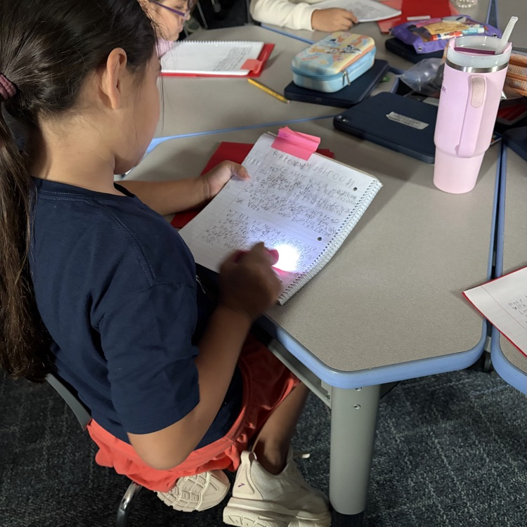 Student using a flashlight to read her writing. 