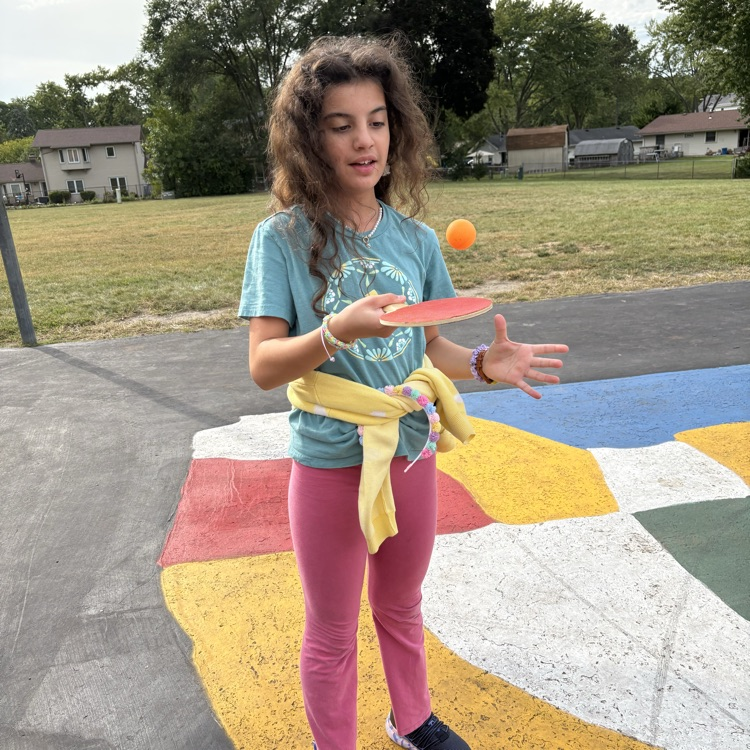 a girl bouncing  her ping pong ball on her paddle 
