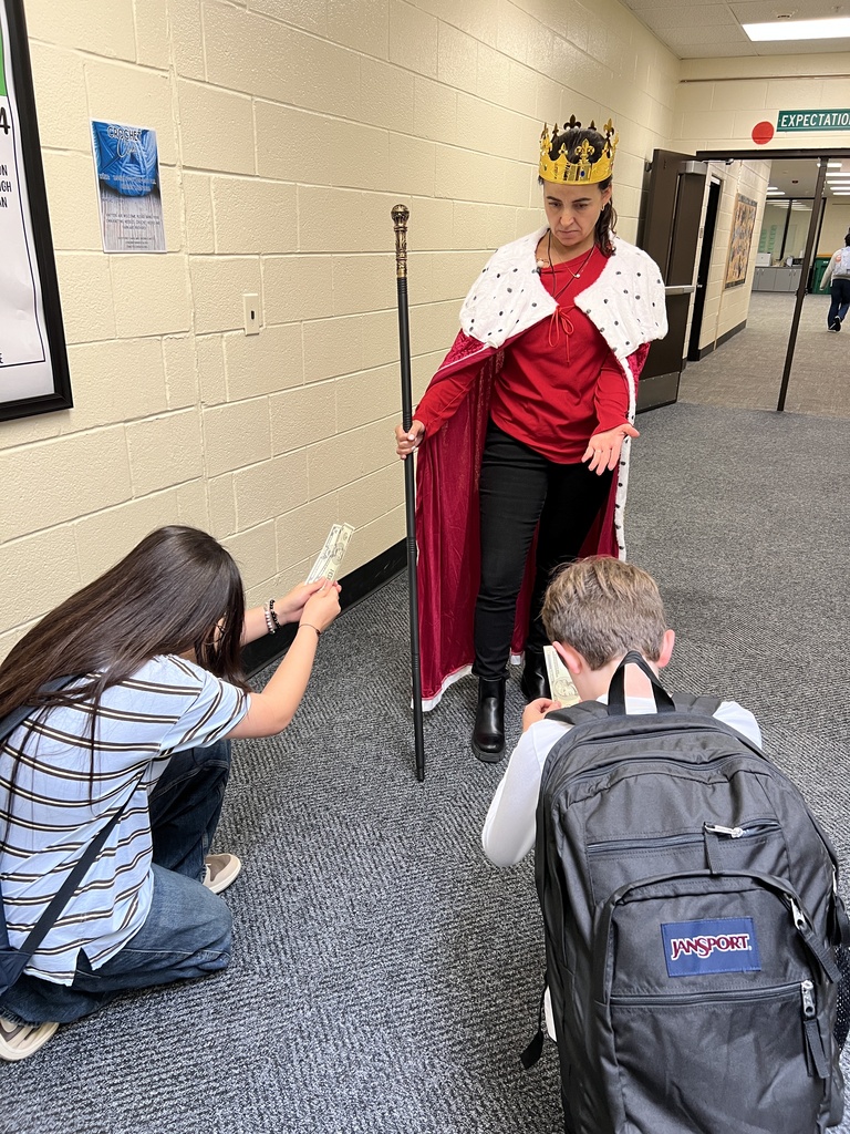 A teacher dressed up as King George III, students are kneeling and providing him with money