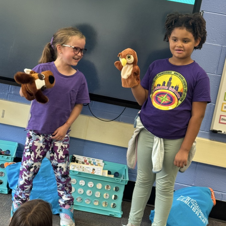 two students holding owl and dog puppets