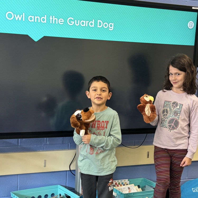two students holding owl and dog puppets 
