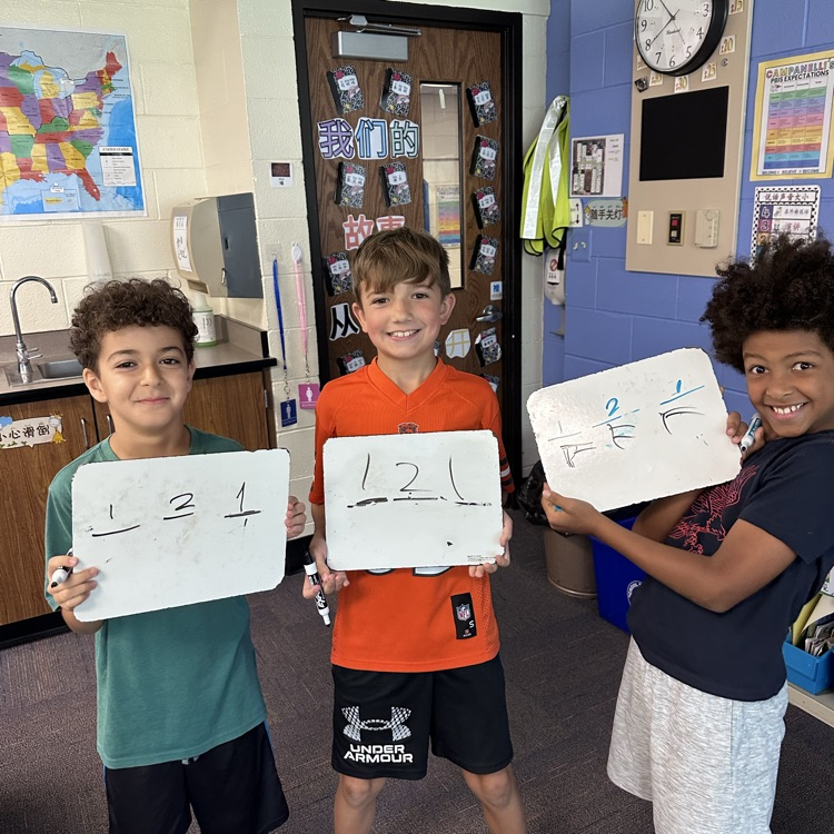 three students holding up whiteboards with numbers 