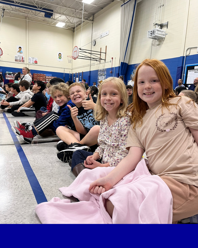 Students smiling sitting on the gym floor for the assembly