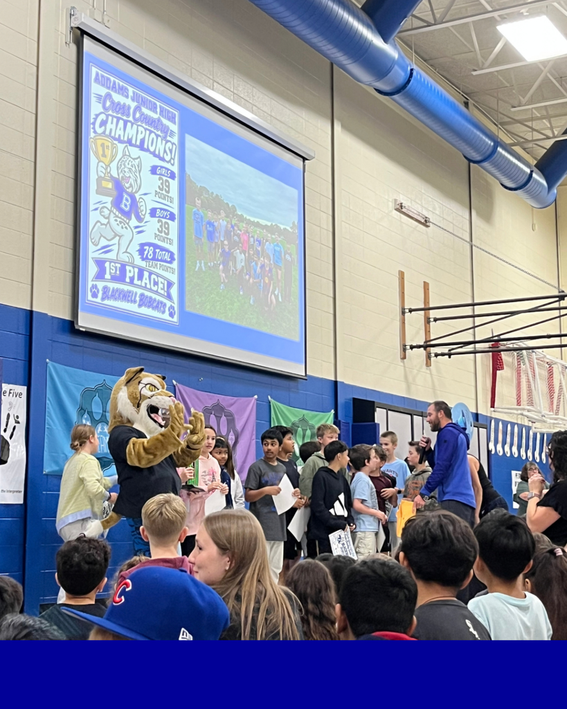 Blackwell Elementary Cross Country Champions at Addams Junior High. Students who ran in the competition at the front of the gym with gym teacher to be celebrated. Bobby the bobcat mascot