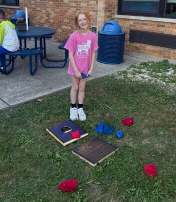 girl standing by a cornhole board and beanbags