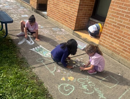 3 students writing with chalk on the sidewalk
