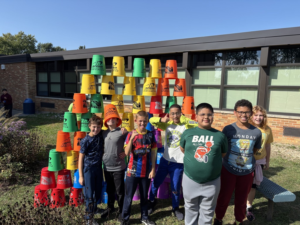 a group of students standing in front of the large cups they stacked