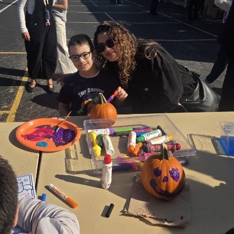 boy with his mom painting a pumpkin and smiling 