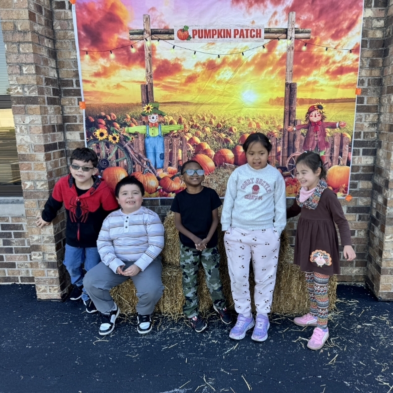 kids taking a group picture outside with hay bales and pumpkins