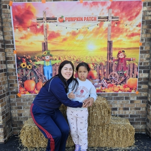 girl with her mom smiling outside in front of hay bales and pumpkins 