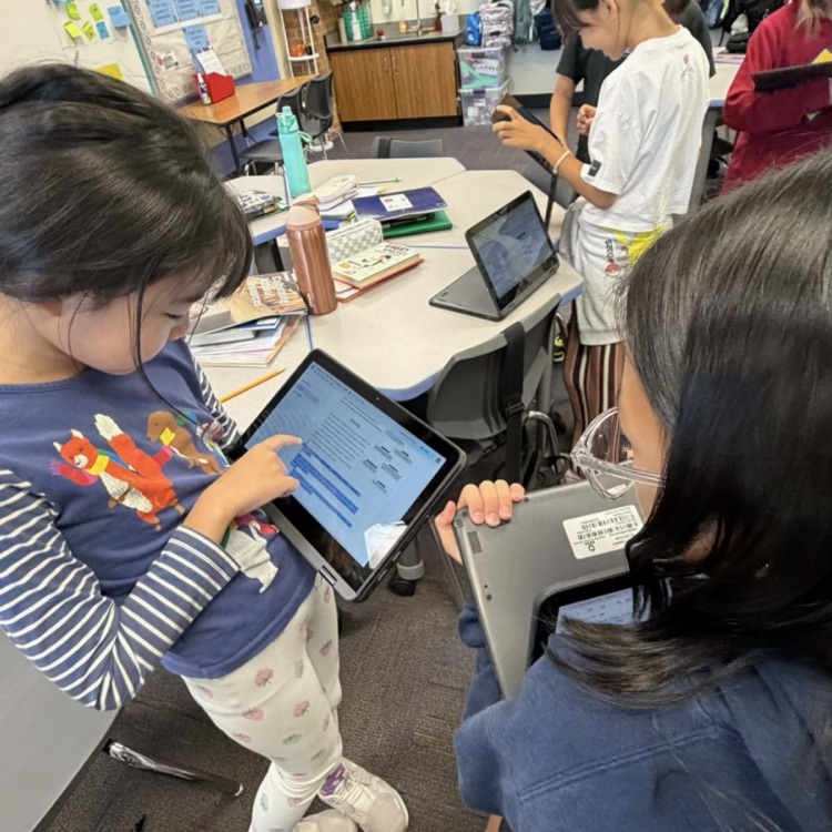 two students looking at writing on their Chromebook