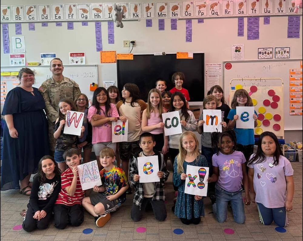 Children stand with teacher and soldier with welcome signs