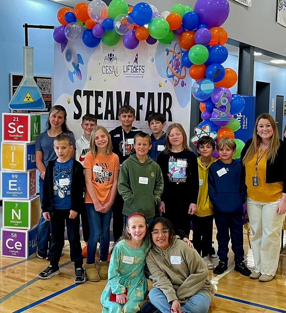 Group of students standing in front of a sign that says "steam fair"
