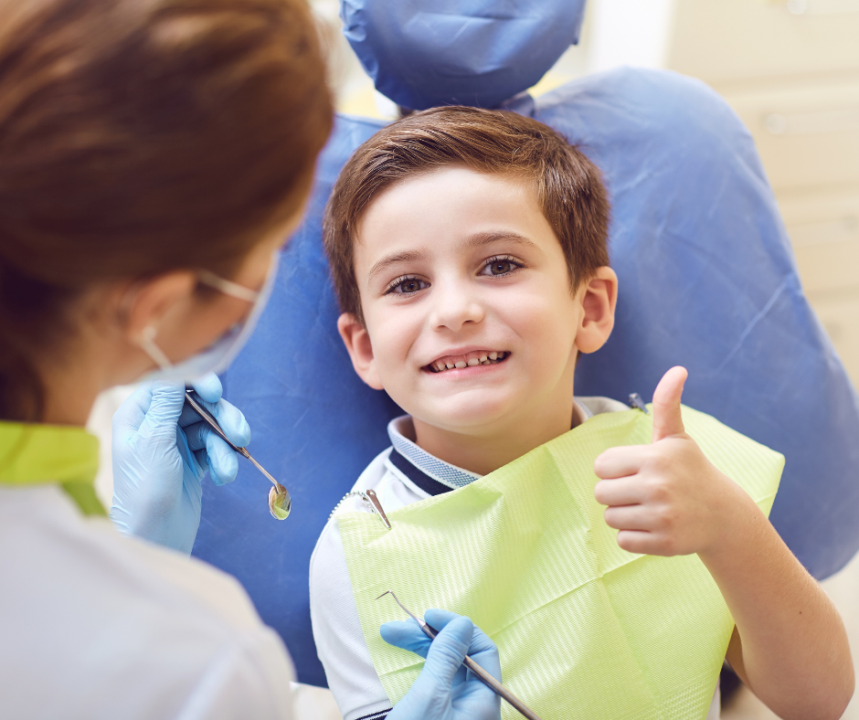 Child holding thumb up while on a dentist chair.