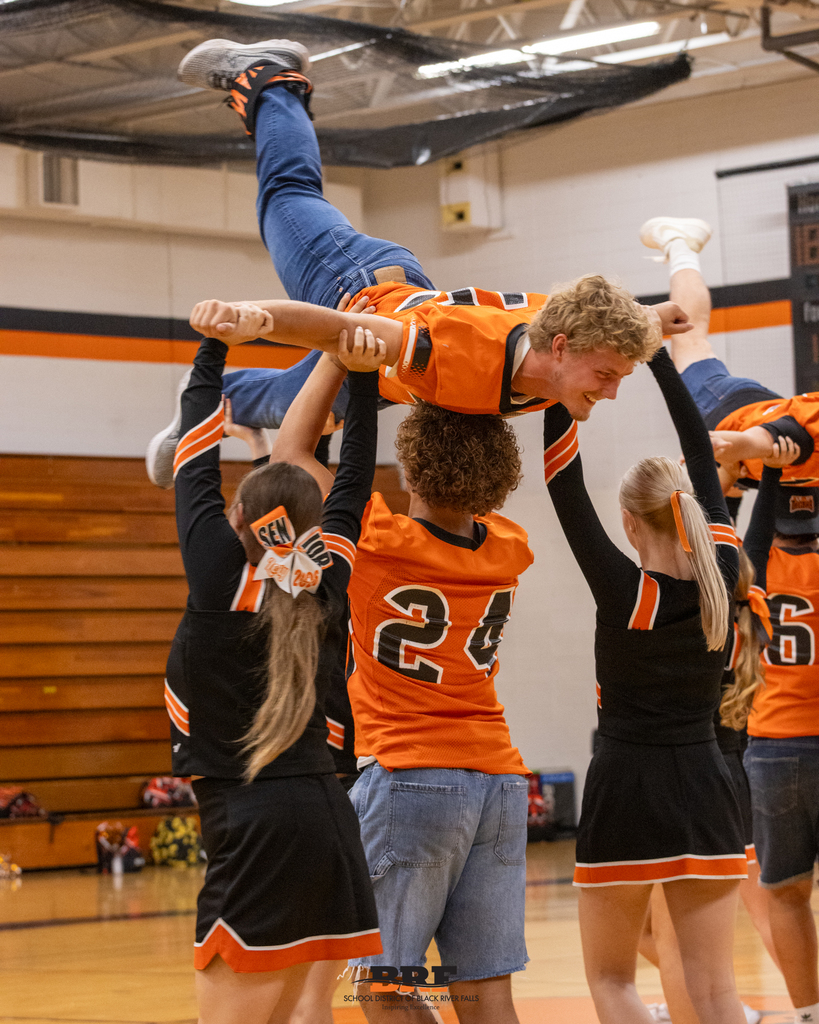 Football player is carried over students shoulders during dance routine.