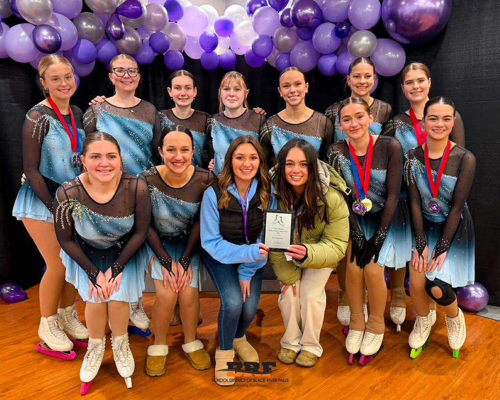 Group of skaters pose for the camera. Two coaches are in the middle, holding a plaque.
