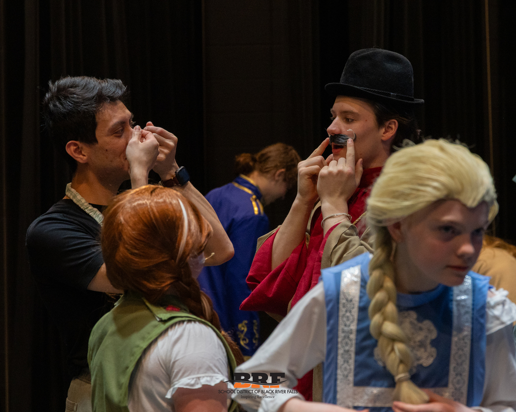 One person showing another how to put on a fake mustache.