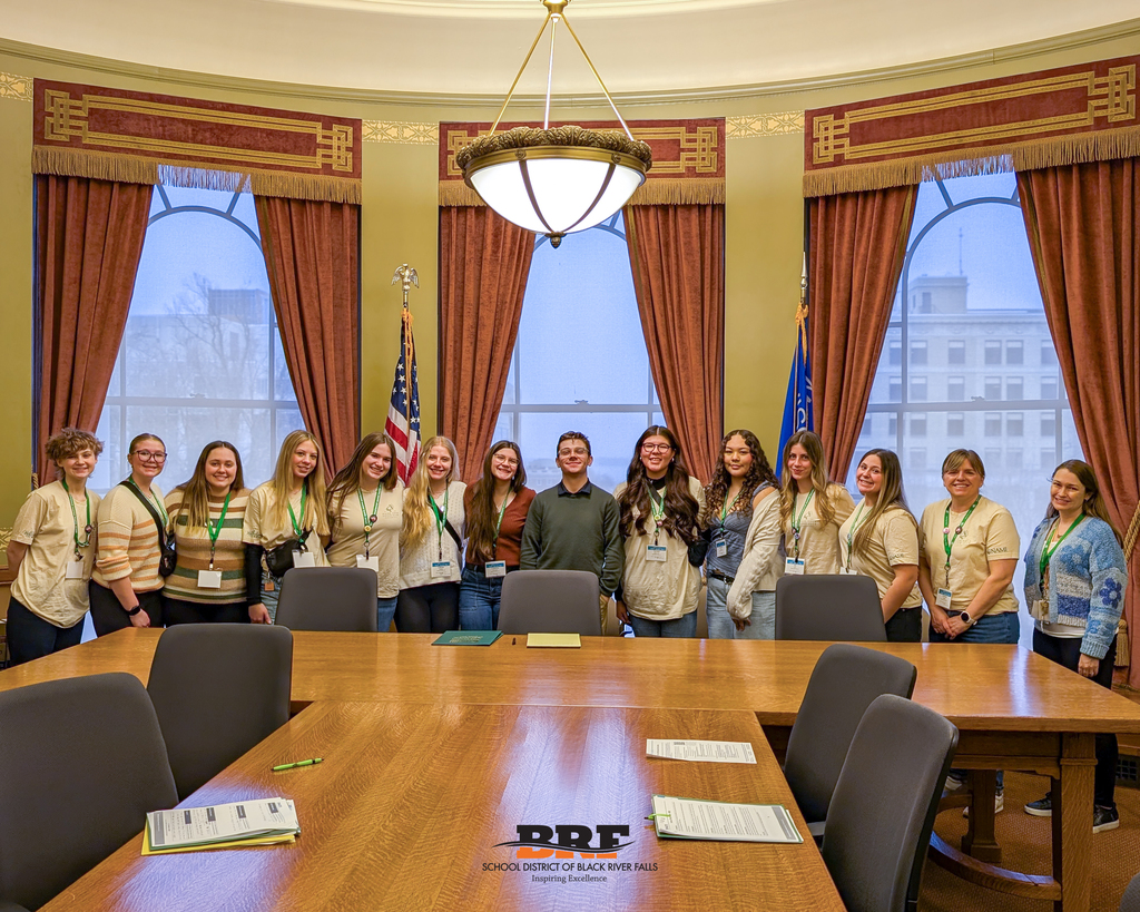 Students standing in an office behind a conference table.