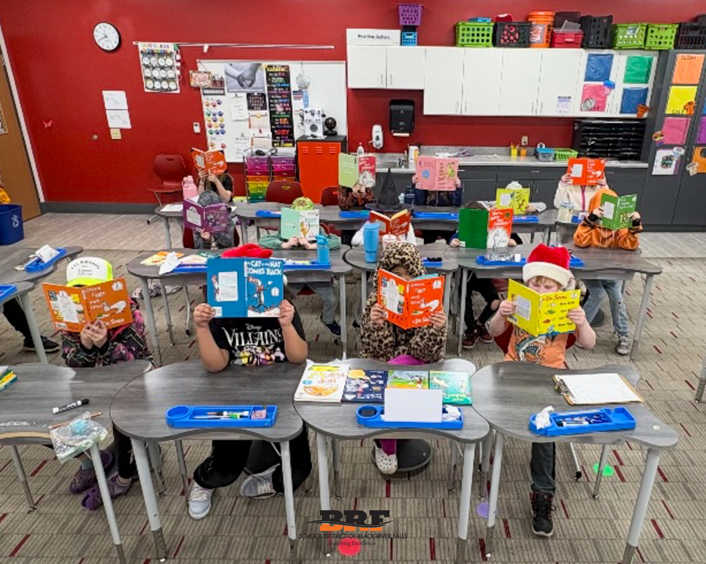 Students sitting at desks, holding Seuss books in front of their faces.