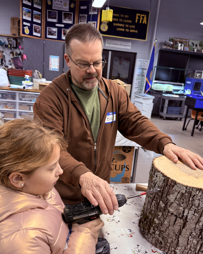 Man helps girl hold a drill to a log