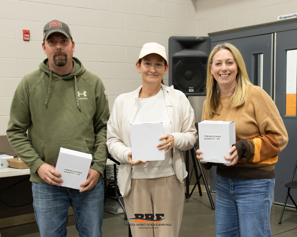 Three people standing in a row, holding boxes.