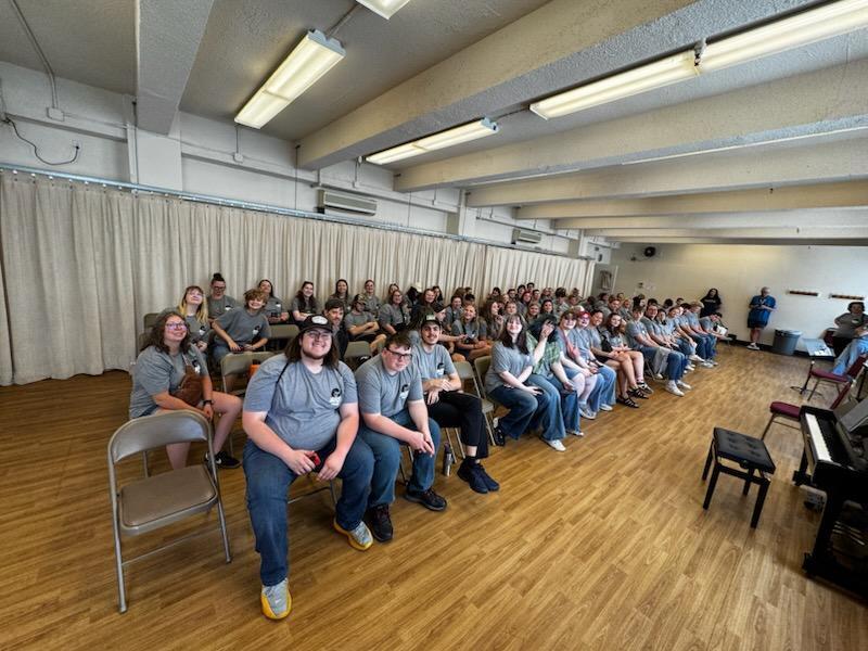 Group of students sit in folding chairs, filling room.