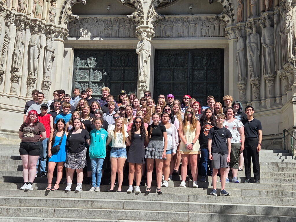 Large group of people stand  on steps in front of building.