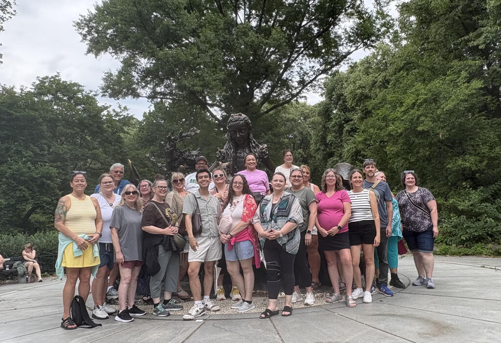 Group of adults stand in front of a statue and tree.