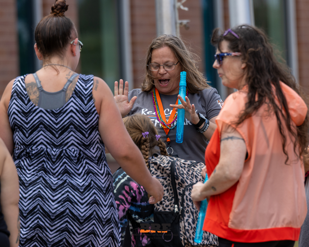 School staff members and families interacting joyfully outdoors with giant bubble wands during open house.