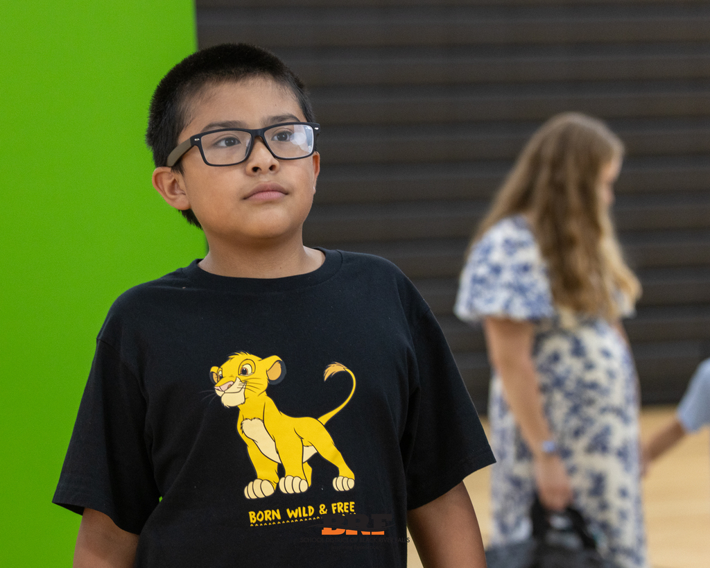 A young boy wearing glasses and a black Simba t-shirt looking forward with a focused expression.