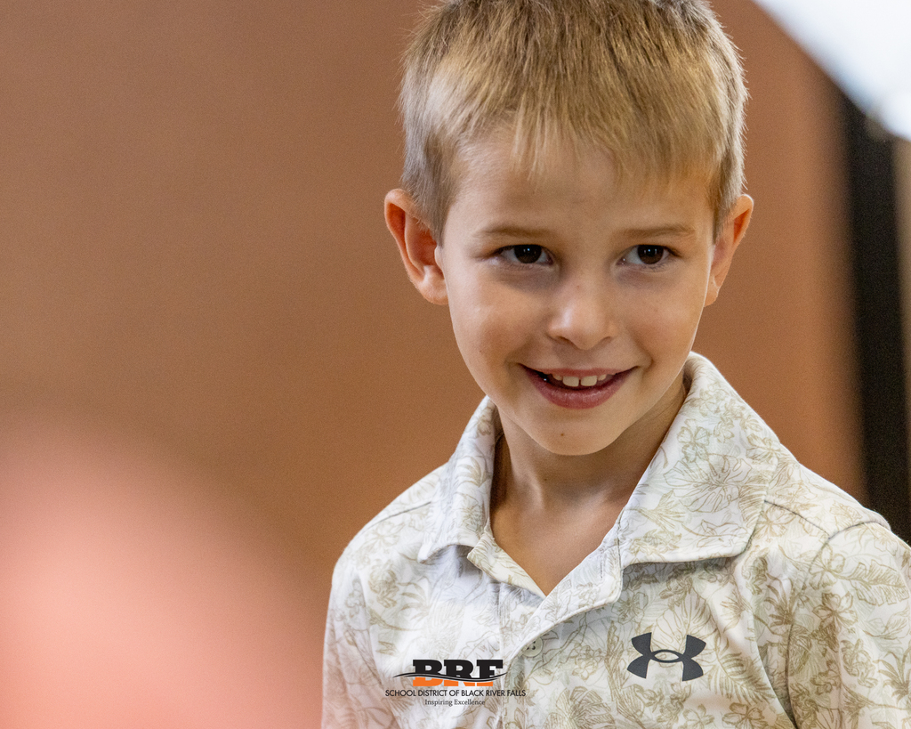 A close-up portrait of a young boy wearing a printed collared shirt, smiling softly off-camera.
