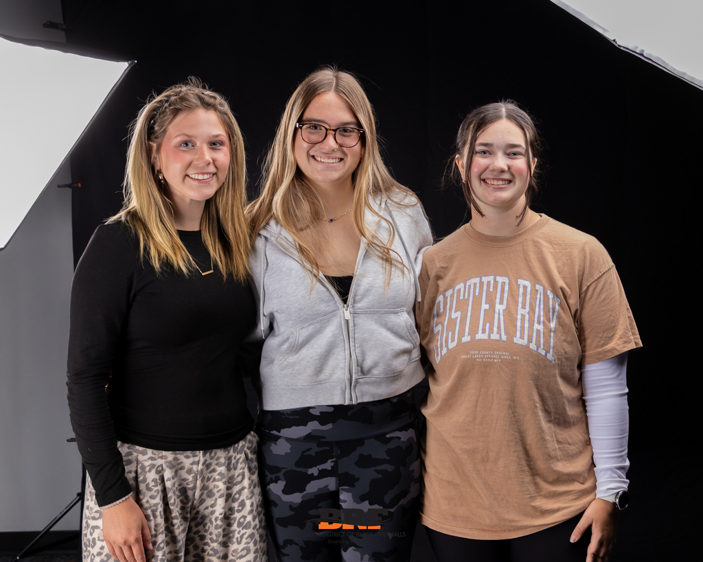 Three girls standing in a group, smiling.